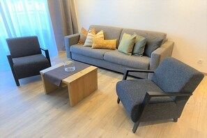 A living room with a grey sofa, two armchairs, a wooden coffee table, and a glass on the table. - Apart Sopherl 5-8 PAX (Pettneu)