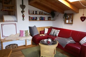 A cozy living room with a red sofa, a wooden coffee table, and a bookshelf filled with books. - Holiday apartment with 2 bedrooms (Hochkrimml)