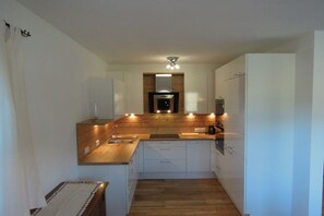 A compact kitchen with a central island, built-in appliances, and a wooden backsplash. - in Chalet Achenkirch (Achenkirch)