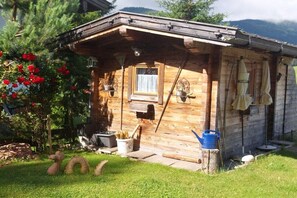 A rustic wooden cabin with a porch, a window, and a small garden area with a watering can. - in Chalet Achenkirch (Achenkirch)