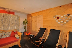A room with a wooden wall, a sofa, two lounge chairs, a potted plant, and a heart-shaped decoration. - Villa Natur - a different kind of living (Schröcken)