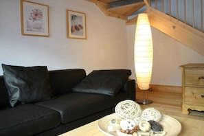 Una sala de estar moderna con un sofá negro, piso de madera, una lámpara y objetos decorativos sobre una mesa.