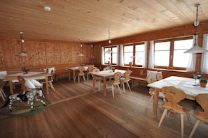 A wooden interior with multiple dining tables and chairs, large windows, and hanging pendant lights. - Villa Natur - a different kind of living (Schröcken)