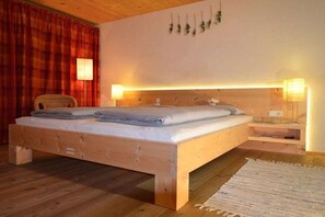 A wooden bed with a headboard, a bedside table with a lamp, and a chair. - Villa Natur - a different kind of living (Schröcken)