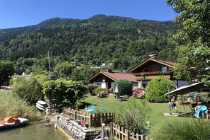 A lakeside property with a wooden cabin, a small dock with boats, and a mountain backdrop. - Seehäuser Ramsbacher Haus 2 (Sattendorf)