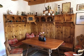 Un comedor de madera con una mesa y bancos, estantes con adornos y una lámpara colgante.