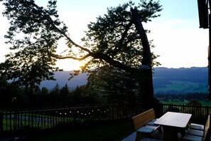 Eine Terrasse mit Tisch und Bänken, mit Blick auf ein Tal, im Vordergrund steht ein Baum.