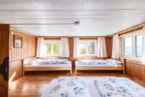 Ein Zimmer mit zwei hölzernen Betten, großen Fenstern und einer Holzbalkendecke.