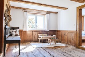 Ein Zimmer mit Holzboden, einer Bank mit einem Deer-Kissen, einem Tisch mit Stühlen und einem Fenster mit Vorhängen.