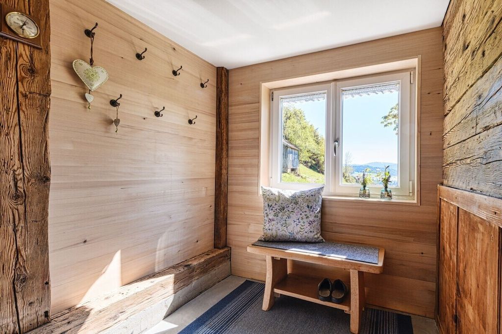 Een houten interieur met een bank, een raam met uitzicht en wandhaakjes.