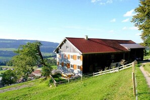 Ein zweistöckiges Gebäude mit rotem Dach, gelegen auf einem grasbewachsenen Hügel mit Blick auf die Landschaft.