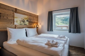 A double bed with white linens, a painting on the wall, and a window with curtains. - Apartment in Niedernsill with swimming pool (Niedernsill)