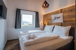 Een hotelkamer met een bed, een raam met gordijnen, een houten hoofdeinde en een aan de muur hangend schilderij.