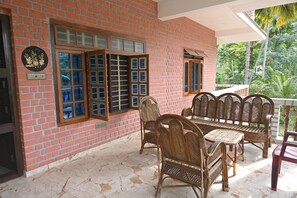 A room with a brick wall, a window with multiple panes, a wooden door, and a seating area with wicker furniture. - Relaxing Holiday Villa in Santhapuram, Kanyakumari (Nagercoil)