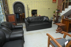 A living room with a black leather sofa, a wooden coffee table, and a staircase leading to an upper level. - Relaxing Holiday Villa in Santhapuram, Kanyakumari (Nagercoil)