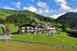 A hotel with multiple buildings, a well-maintained lawn, and a mountainous backdrop. - Holiday apartment with 3 bedrooms (Riezlern)