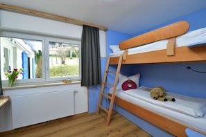 A bunk bed room with a window, a radiator, and a small table with a vase of flowers. - Holiday apartment with 3 bedrooms (Riezlern)