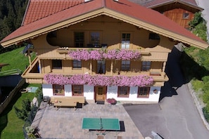 A two-story building with a balcony, a green tennis court, and a red roof. - Holiday apartment with 2 bedrooms (Hippach)