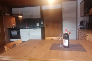 A kitchen with wooden cabinets, a dining table with a placemat, a wine bottle, and glasses. - Holiday apartment with 2 bedrooms (Hippach)
