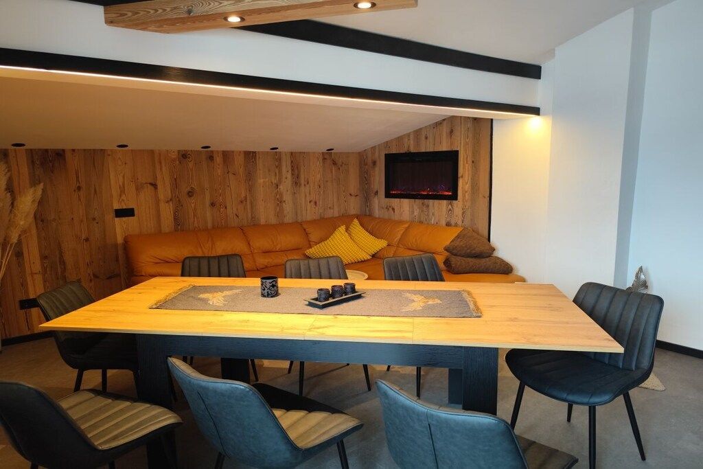 A modern dining area with a wooden table, blue upholstered chairs, and a sofa with cushions.