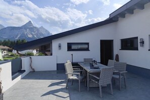 An outdoor patio with a dining table and chairs, a mountain view, and a modern building with large windows. - Apartment in Ehrwald with swimming pool (Ehrwald)