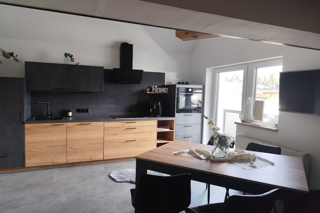 A modern kitchen with dark cabinetry, a wooden dining table, and a built-in oven.