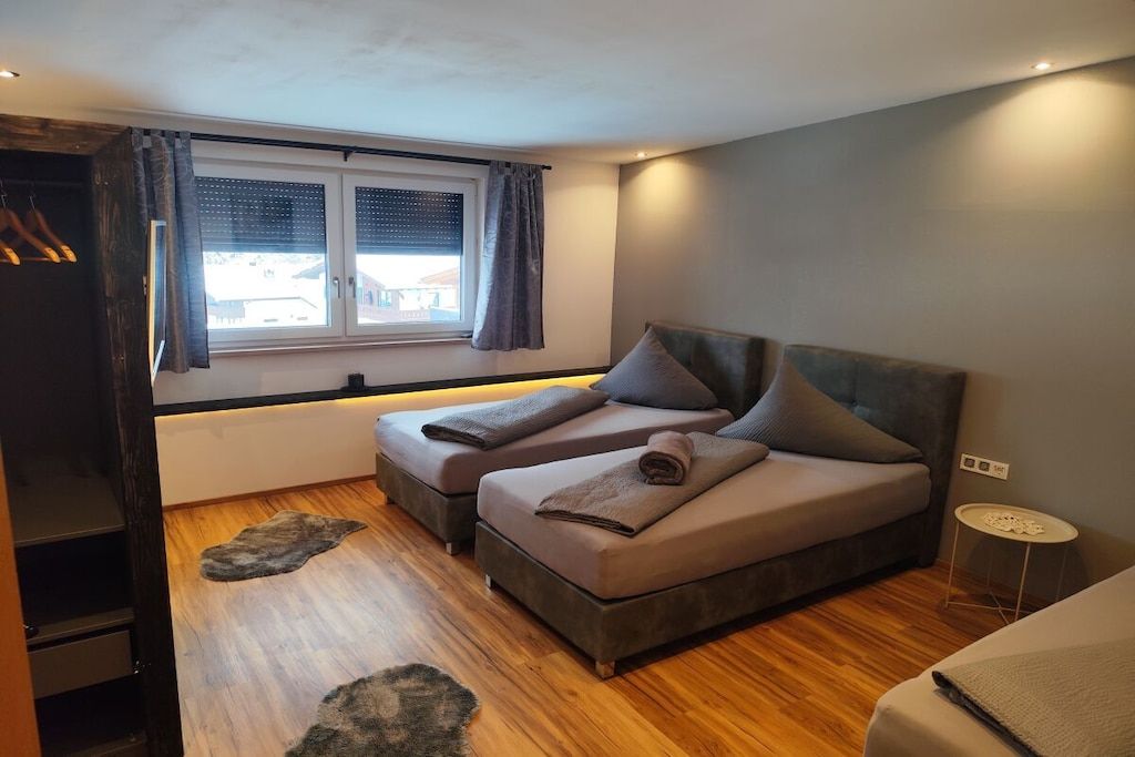 A bedroom with two beds, a window with curtains, a small round table, and a wooden floor.