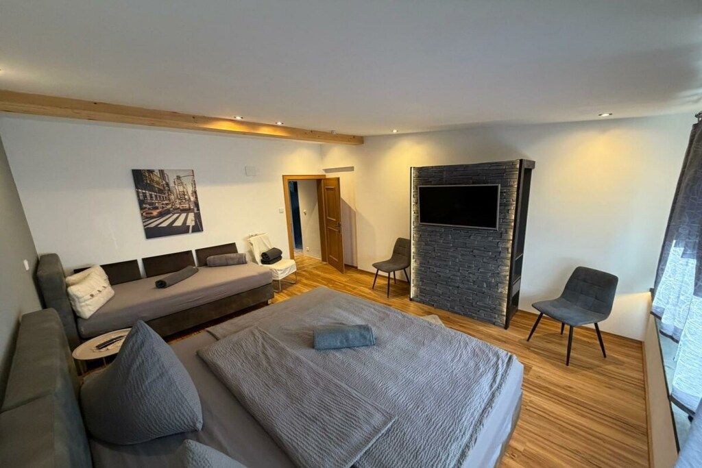 A modern bedroom with a bed, a sofa, a TV, and a chair.