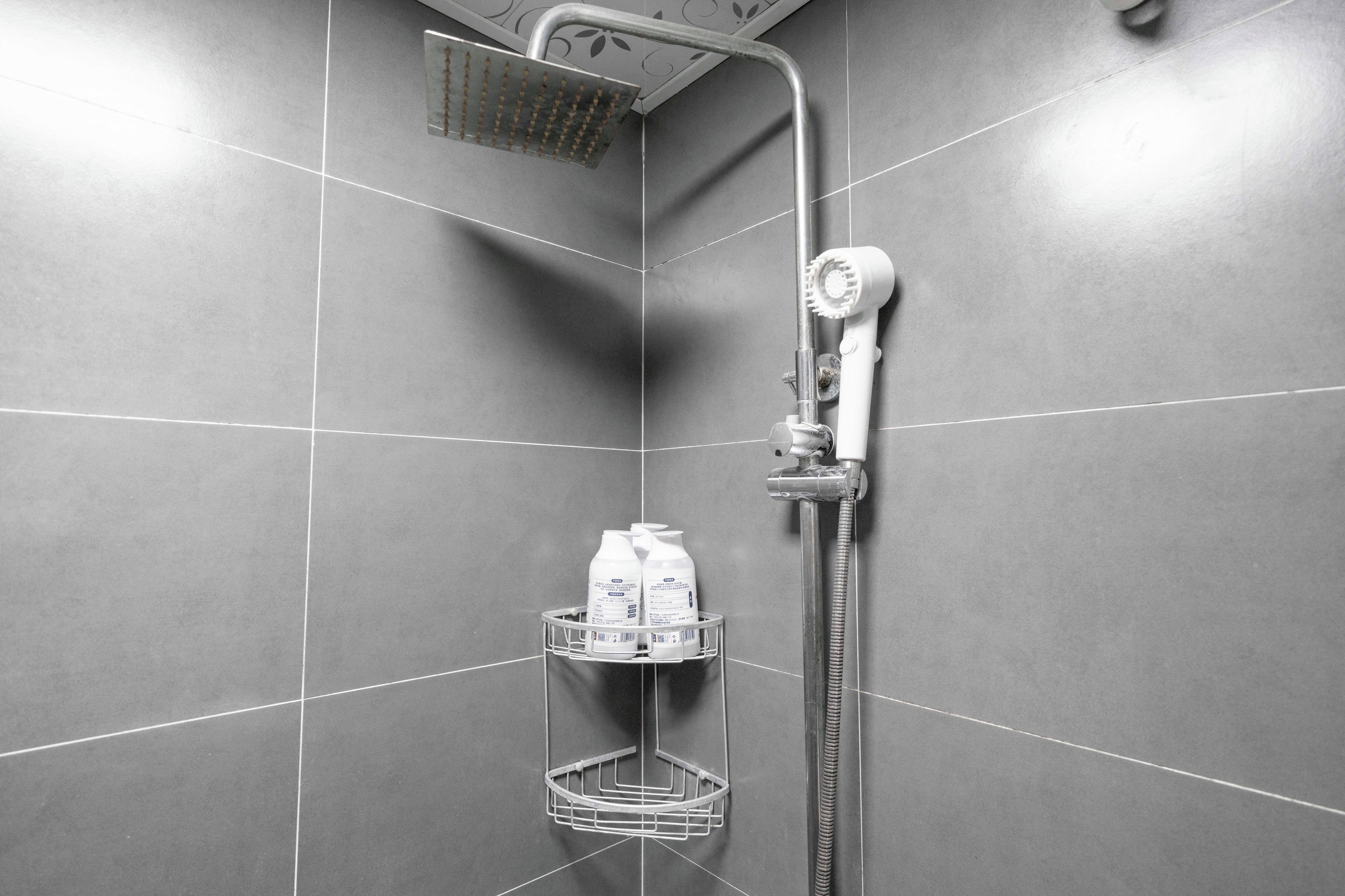 Eine Dusche mit Handbrause und Wandarmatur, ein weißer Handtuchhalter mit Flaschen sowie eine Duschwanne aus Metall.