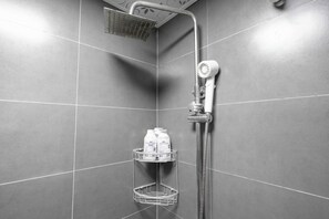 A shower with a handheld showerhead and a wall-mounted faucet, a white towel rack with bottles, and a metal shower tray. - Book&Bed-The Bund Tiantong Road Branch (Shanghai)