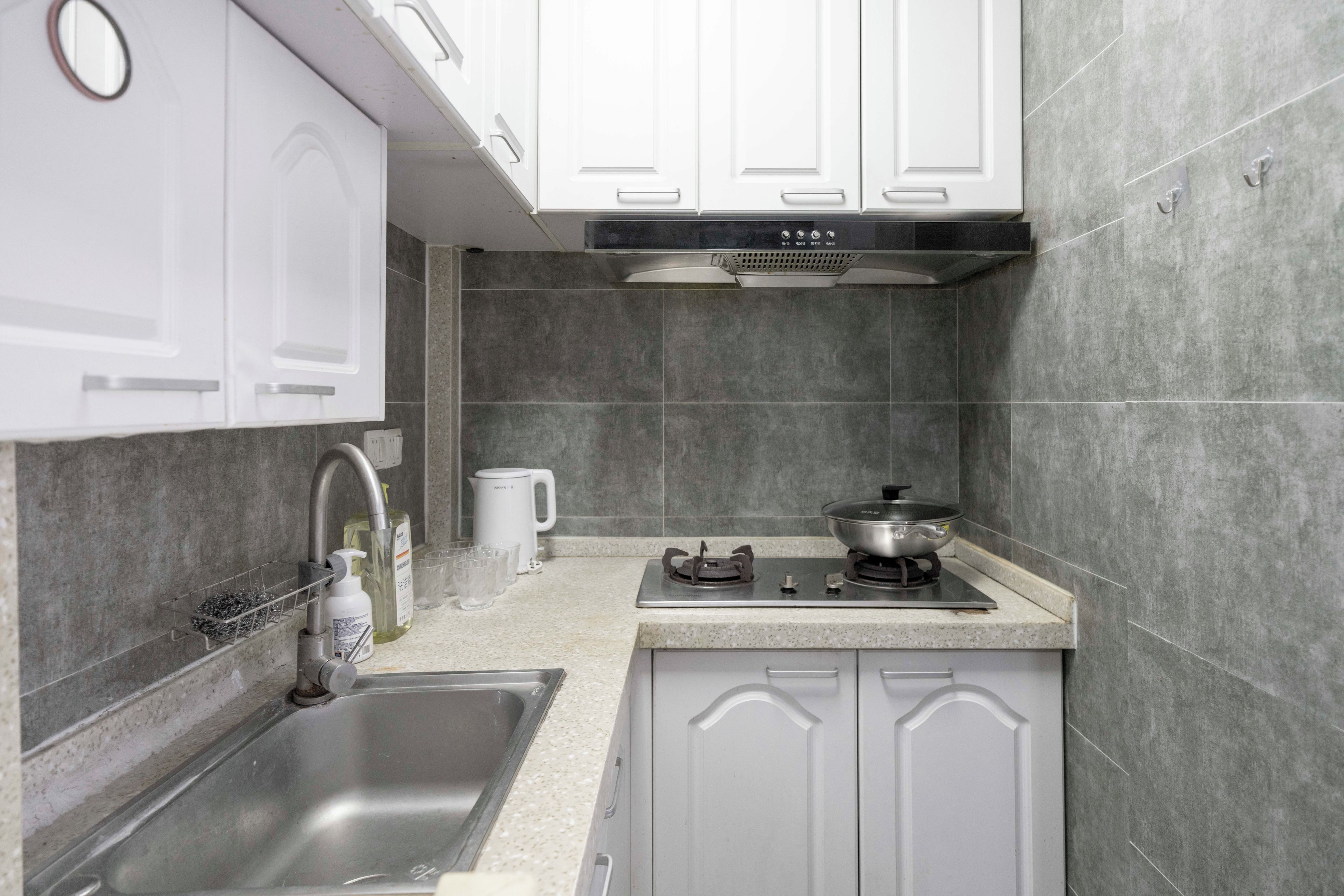 A modern kitchen with white cabinets, a stainless steel sink, a gas stove, and a coffee maker.