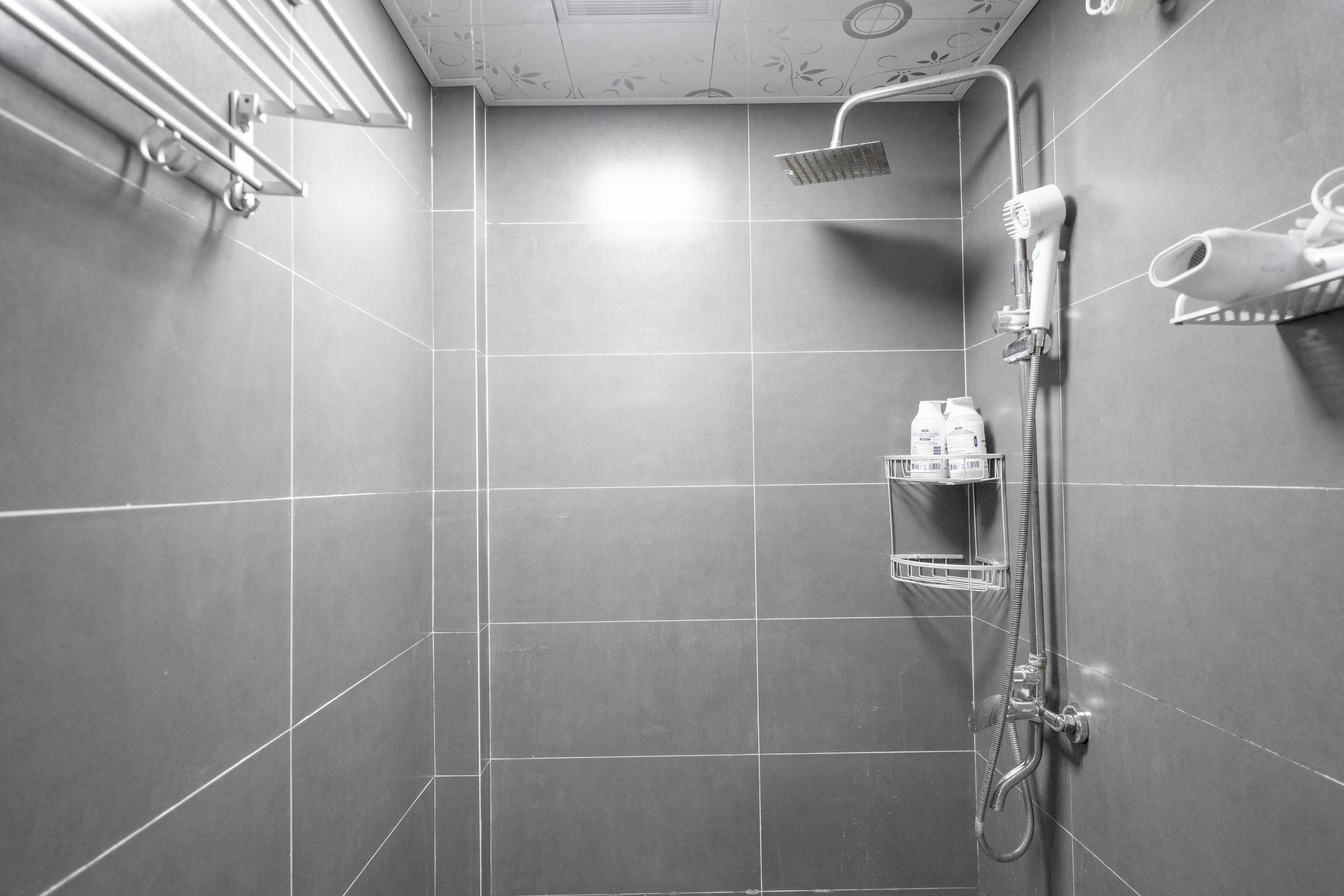 A modern shower area with a handheld showerhead, a wall-mounted hairdryer, and a shelf with toiletries.