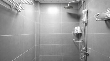 Un espacio de ducha moderno con un cabezal de ducha de mano, un secador de pelo fijado a la pared y un estante con artículos de aseo.