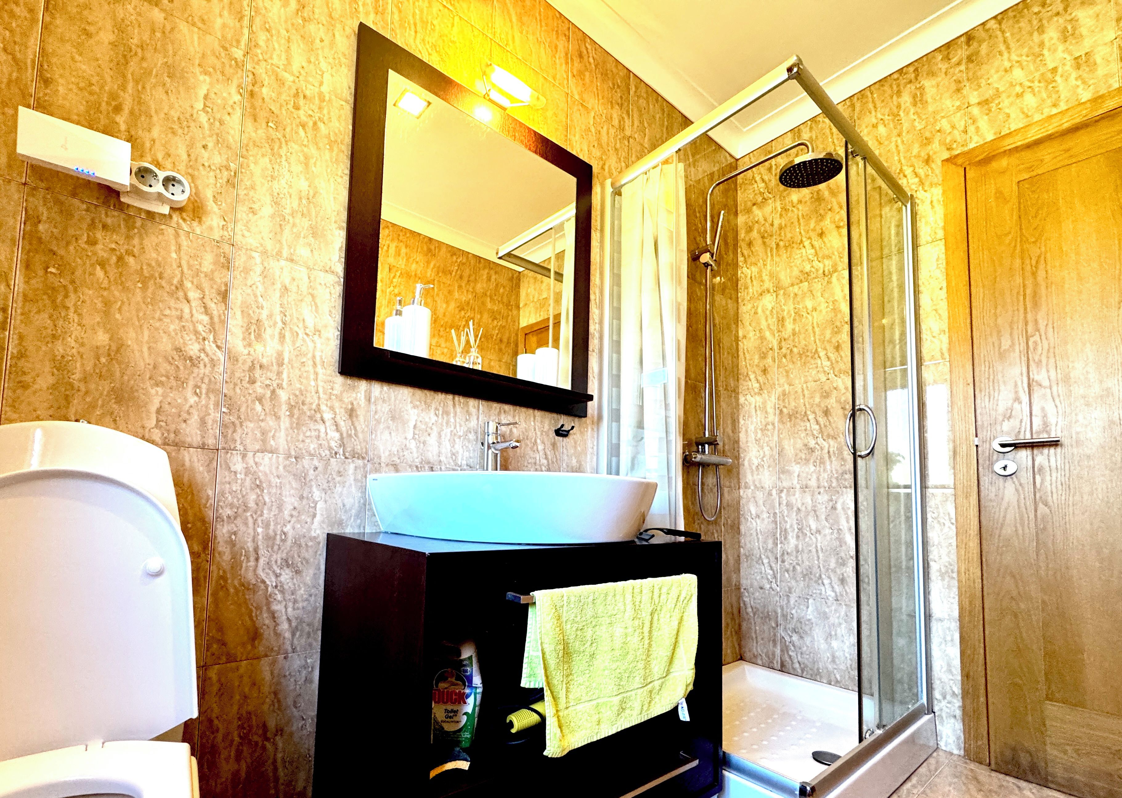 A bathroom with a toilet, sink, mirror, shower, and a towel rack.