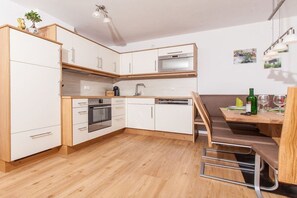 A modern kitchen with white cabinetry, a built-in oven, and a dishwasher. There is a dining area with a wooden table and chairs. - Holiday apartment in Rauris with sauna (Rauris)