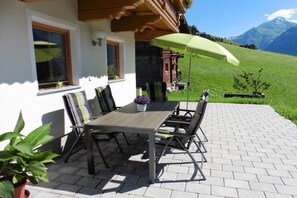 An outdoor patio with a wooden table and chairs, a green umbrella, and a view of a mountain. - Holiday apartment in Rauris with sauna (Rauris)
