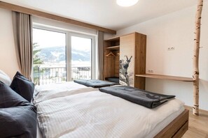 Ein Schlafzimmer mit einem großen Bett, einem Holzschrank, einem kleinen Schreibtisch und Blick ins Freie.