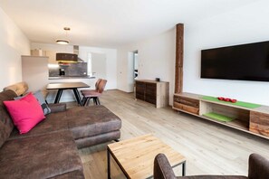 Ein stilvoller Wohnraum mit Sofa, Couchtisch, Fernseher und einer Küchenzeile im Hintergrund.