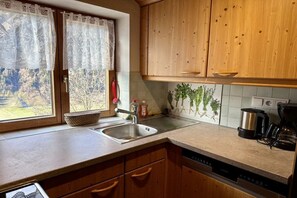 Een keuken met houten kasten, een roestvrijstalen spoelbak en een koffiezetapparaat, met uitzicht op de omgeving.