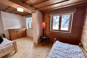 A wooden cabin bedroom with two beds, a small table, and a window with a view of snow-capped mountains. - Holiday home in Rauris with sauna (Rauris)