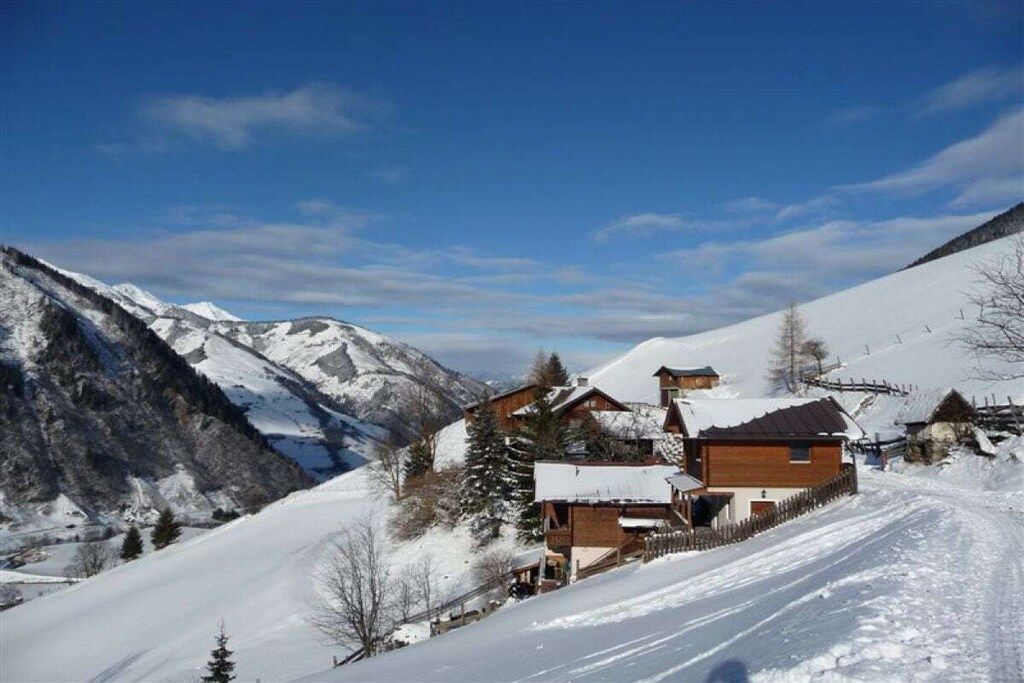 A snow-covered mountain landscape with a wooden chalet-style building with a sloped roof and a wooden fence.