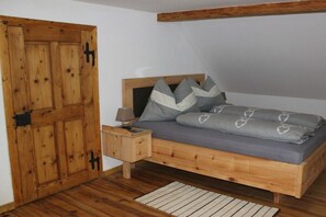 Ein Schlafzimmer mit Holztür, einem Bett mit grauer Bettwäsche, einem Nachttisch und Holzboden.