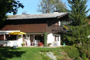 A two-story house with a covered patio area, outdoor seating, and a garden. - Holiday home with 1 bedroom (Kirchberg in Tirol)