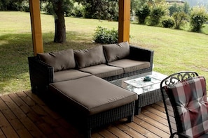 A wicker sofa with cushions on a wooden deck, a glass table, and a chair with a plaid cushion. - Holiday alpine house (St. Georgen)