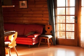 Een gezellige kamer met een rode bank, een houten stoel en een raam met gordijnen.