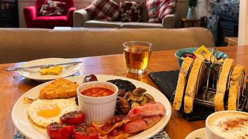 A breakfast setting with a plate of eggs, bacon, tomatoes, beans, toast, and a cup of tea.