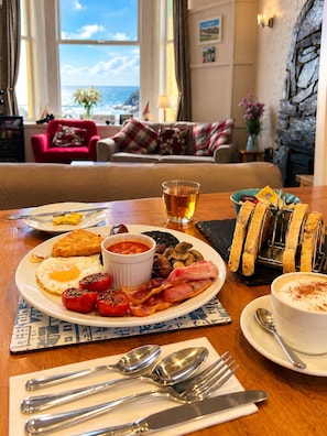 A breakfast setting with a plate of eggs, bacon, tomatoes, beans, toast, and a cup of tea. - Awel Mor (Criccieth)