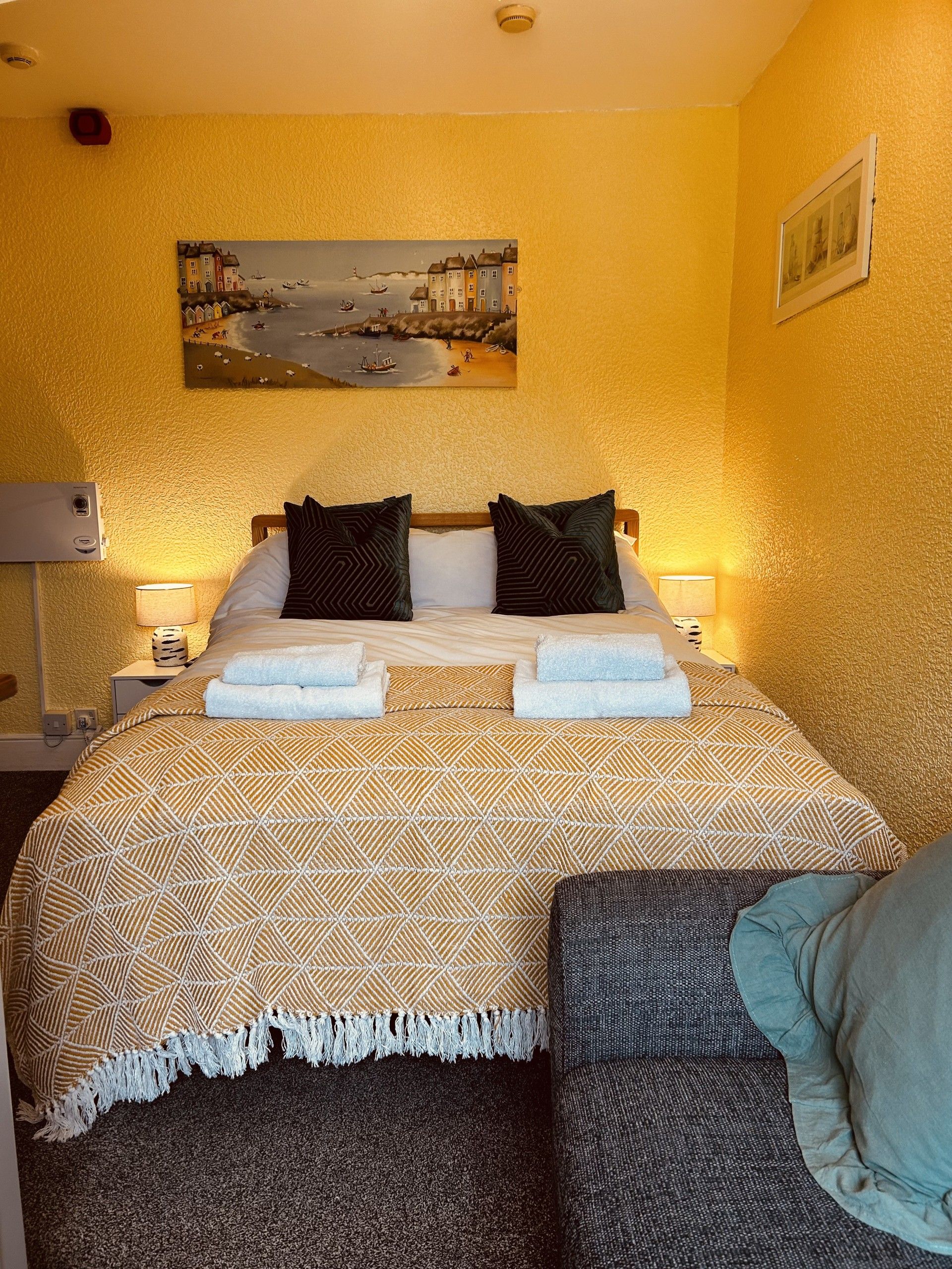 A hotel room with a bed, two bedside lamps, a painting on the wall, and a small table with a lamp.