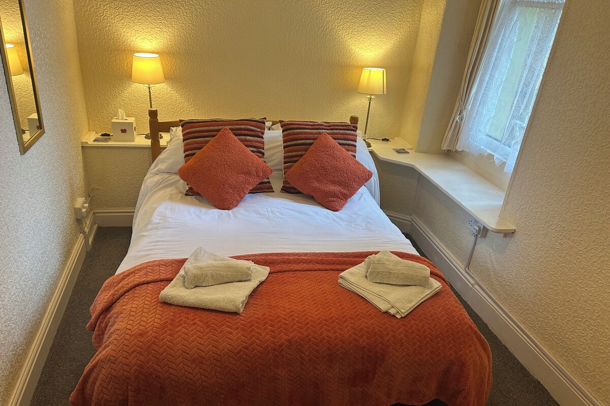 A hotel room with a bed, two bedside lamps, a window, and a nightstand with a lamp.