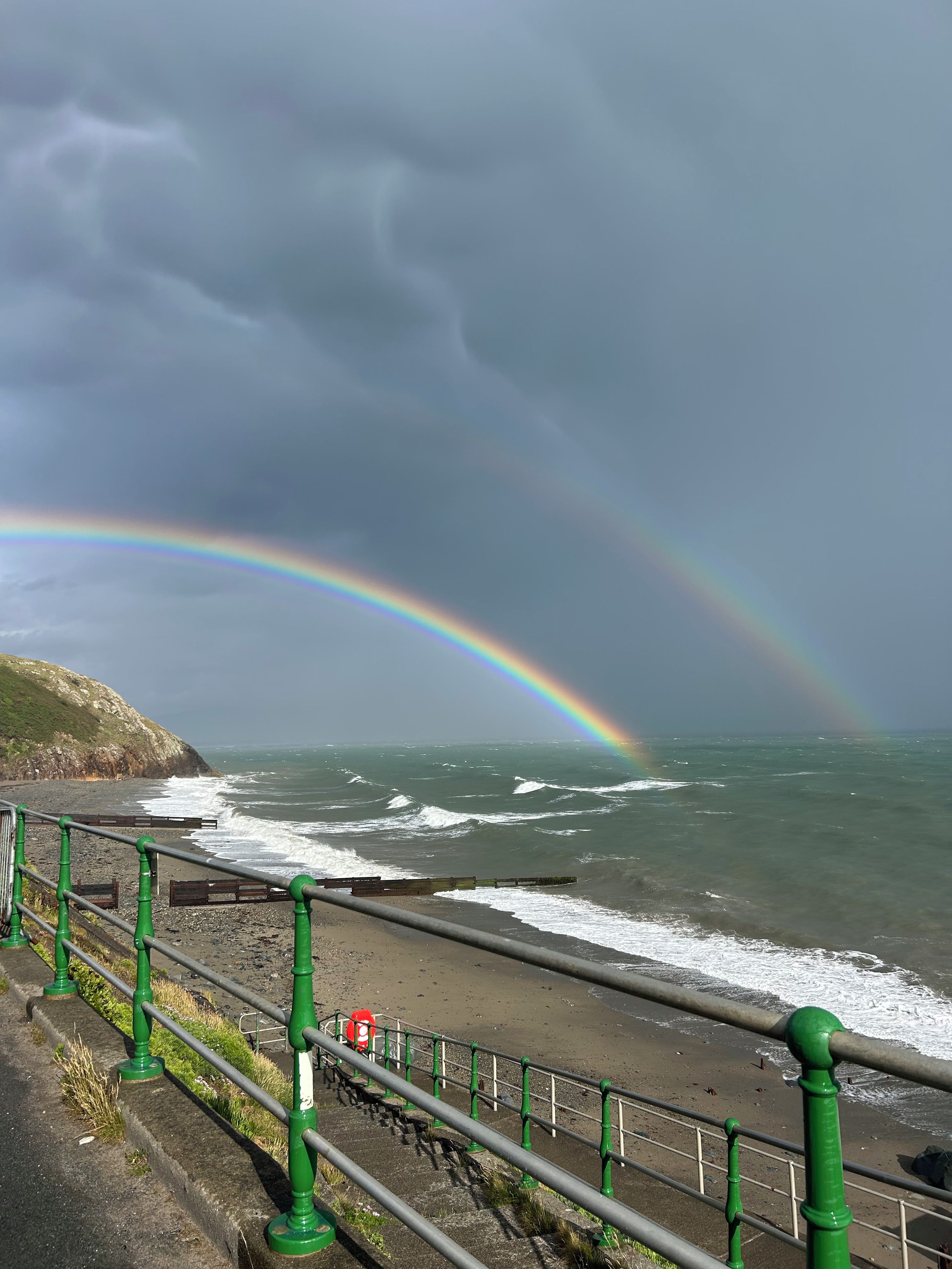 A coastal scene with a rainbow, waves, and a railing.
